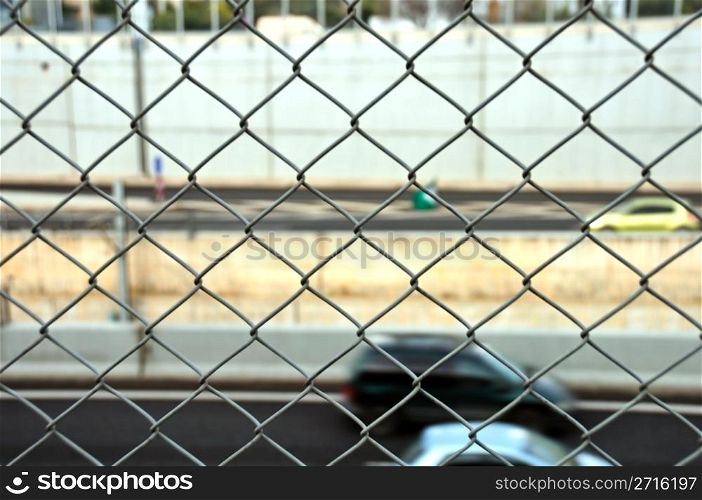 Speeding cars on the motorway seen through wire mesh fence. Motion blur.