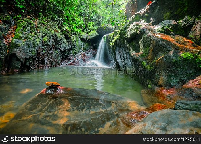 Spellbinding pond with waterfall in middle of jungle. Mysterious pool in thick tropical forest with running water falling into lake surrounded by wild vegetation and rocks. North Sumatra, Indonesia.