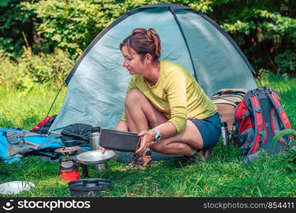 Spending a vacation on camping. Woman preparing a meal outdoor next to tent