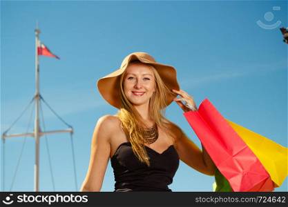 Spending money, buying things concept. Portrait of attractive elegant woman holding shopping bags wearing glamorous outfit with clear blue sky and polish flag in background. Portrait of elegant woman with shopping bags