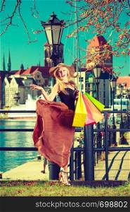 Spending money on sales, buying things concept. Fashionable woman relaxing and standing with shopping bags in town, wearing windblown long dress and sun hat. Fashionable woman walking with shopping bags