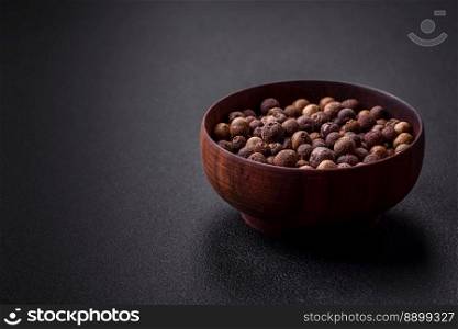 Spice allspice brown color not ground in a wooden saucer on a dark concrete background