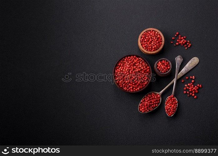 Spice, allspice peas in red or pink color in a wooden bowl on a black concrete background. Asian cuisine