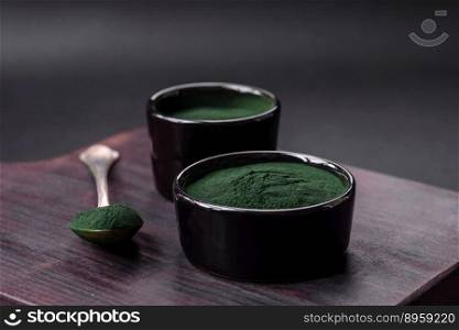 Spice, green color spirulina in the form of powder in a black bowl on a dark concrete background