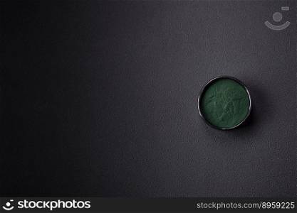 Spice, green color spirulina in the form of powder in a black bowl on a dark concrete background