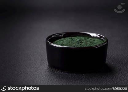 Spice, green color spirulina in the form of powder in a black bowl on a dark concrete background