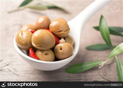 Spiced olives in spoon on wooden background. Spanish tapa