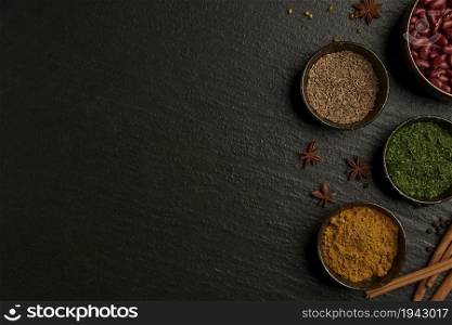 spices concept the varieties of colors and types of spices set into small bowl on the black background with a wooden spoon.