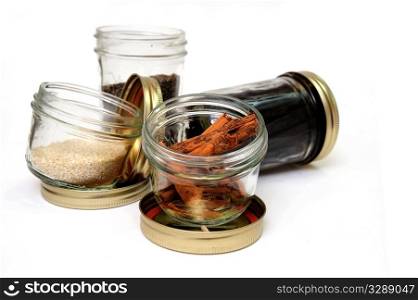 Spices. Glass jars of stick cinnamon, vanilla beans, black pepper and sesame seeds on an isolated background