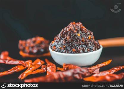 Spicy chili paste in white ceramic container on dark background