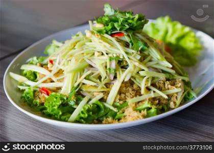spicy crispy catfish salad with green mango and fresh vegetable on white plate