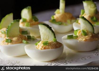 Spicy deviled eggs garnished with cucumber and leek on white plate.. Spicy deviled eggs garnished with cucumber and leek on white plate