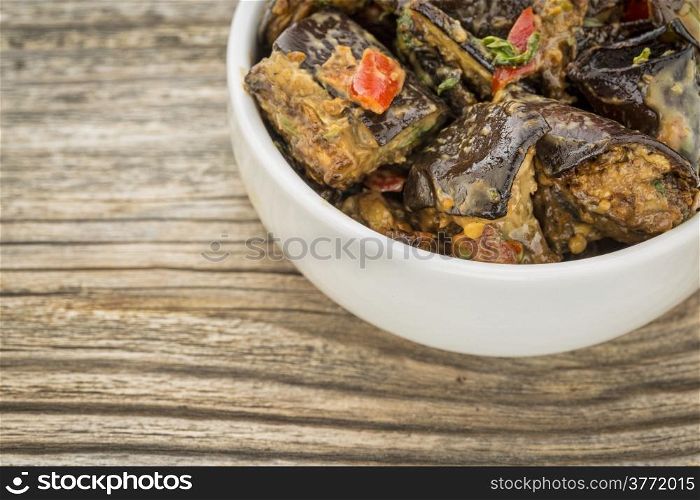 spicy eggplant salad with bell pepper - a small white bowl on a grained wood
