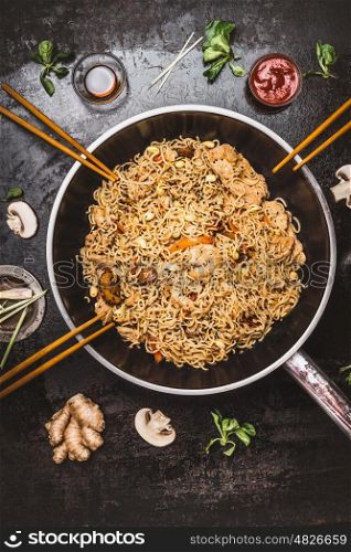 Spicy fried noodles in wok pan with chopsticks on dark rustic background, top view. Asian cuisine