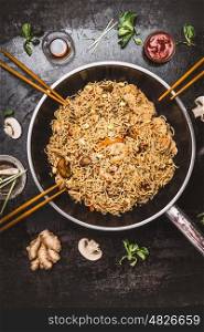 Spicy fried noodles in wok pan with chopsticks on dark rustic background, top view. Asian cuisine