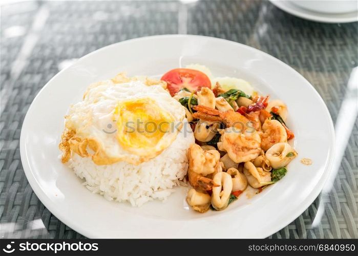 Spicy fried seafood with basil leaves on jasmine rice and fried egg