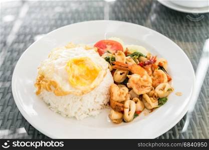 Spicy fried seafood with basil leaves on jasmine rice and fried egg