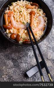 spicy instant noodles soup with shrimps and mushrooms. served by black chopsticks.