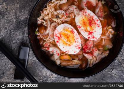 spicy instant noodles soup with shrimps, egg and mushrooms. served by black chopsticks. flat lay. close up
