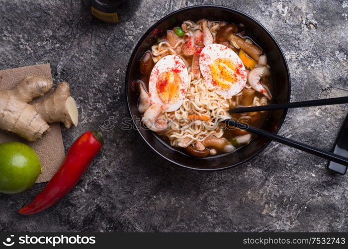 spicy instant noodles soup with shrimps, egg and mushrooms. served by black chopsticks. flat lay