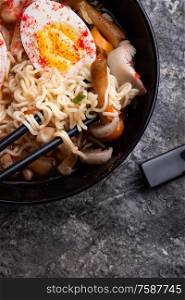 spicy instant noodles soup with shrimps, egg and mushrooms. served by black chopsticks. flat lay. close up
