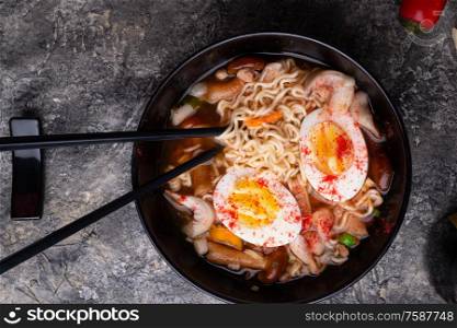 spicy instant noodles soup with shrimps, egg and mushrooms. served by black chopsticks. flat lay