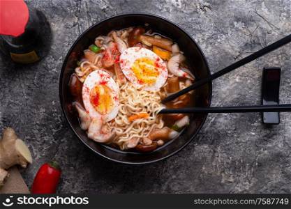 spicy instant noodles soup with shrimps, egg and mushrooms. served by black chopsticks. flat lay
