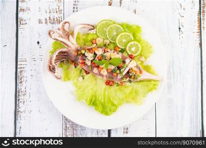 Spicy lemon squid with galangal, chilies, carrots, peppermint, spring onions and garlic on a plate on a white wooden floor.