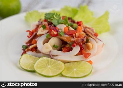 Spicy lemon squid with galangal, chilies, carrots, peppermint, spring onions and garlic on a plate on a white wooden floor.