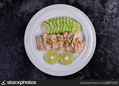 Spicy lime pork salad with bitter melon, galangal, chili, tomatoes and garlic in a white plate on a black cement floor.