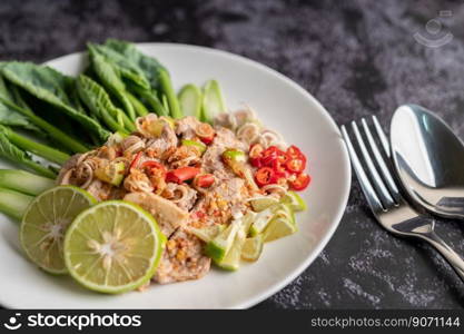 Spicy lime pork salad with kale, galangal, chilli and garlic in a white plate on a black cement floor.