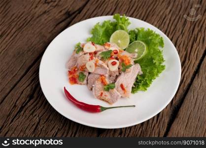 Spicy lime pork with salad, galangal, chilli, tomato and garlic on a white plate on a wooden floor.