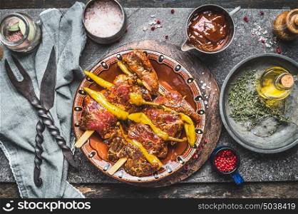 Spicy Meat skewers with green chili pepper on rustic kitchen table background with grill meat fork and knife, oil , seasoning and barbecue sauce, top view
