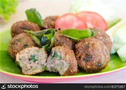 spicy meatballs served with fried bergamot leaves and fresh vegetable on dish