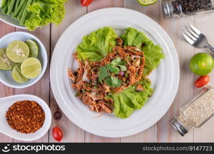 Spicy minced chicken on a white plate complete with cucumber, lettuce and side dishes on wooden table.