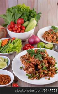 Spicy minced chicken on a white plate complete with cucumber, lettuce and side dishes on wooden table.