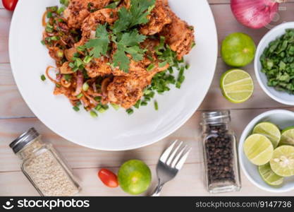 Spicy minced chicken on a white plate complete with cucumber, lettuce and side dishes on wooden table.