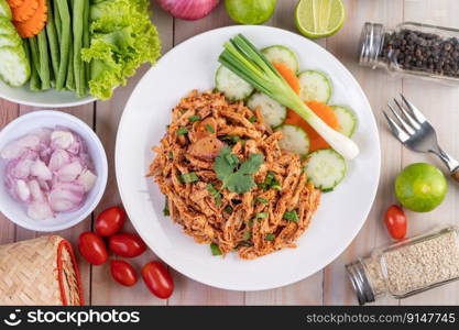 Spicy minced chicken on a white plate complete with cucumber, lettuce and side dishes on wooden table.