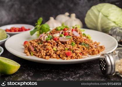 Spicy minced pork salad with chili flakes, lime, chopped green onions, chilli and roasted rice, sliced   shallots on a cement floor.