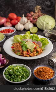 Spicy minced pork salad with chili flakes, lime, chopped green onions, chilli and roasted rice, sliced   shallots on a cement floor.