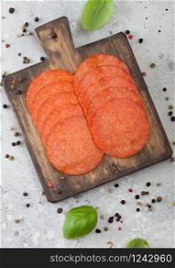Spicy pepperoni salami with basil and pepper on wooden chopping board and light background.
