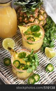 Spicy pineapple margarita with jalapeno slices, lime and cilantro sprigs