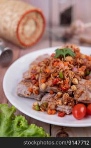 Spicy pork minced with tomatoes and lettuce on a white plate on a wooden table. Selective focus.