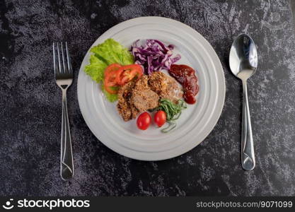 Spicy pork salad with galangal, pepper, tomato, lemon, lime, garlic and salad. Dish on a white ground on a cement floor.