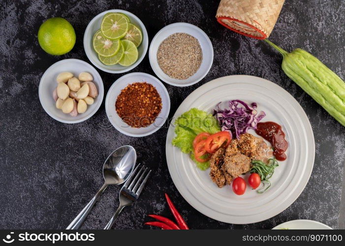 Spicy pork salad with galangal, pepper, tomato, lemon, lime, garlic, salad and bitter melon. Dish on a white ground on a cement floor.