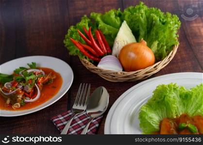 Spicy salad of sardine with tomato sauce arranged nicely in white dish and ingredient herb for cooking put in a wicker basket, Sparken stainless spoon and fork over napkin on wooden table, copy space