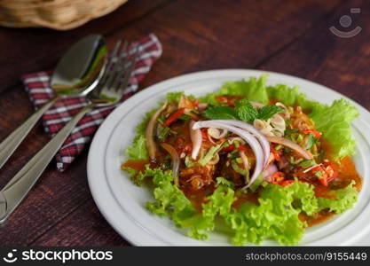 Spicy salad of sardine with tomato sauce mixed with herb in white dish and lettuce leaf in weave basket nearly, the sparken stainless spoon and fork over napkin on wooden table, copy space