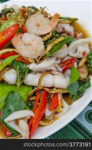 spicy seafood dish , fried shrimp and squid with herbal vegetables on white plate ,