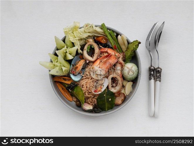 Spicy Stir Fried seafood Instant Noodles with herbs with various spices served with vegetables, cucumber, thai eggplant, chinese cabbage, white turmeric, winged bean and yardlong bean in ceramic plate. Top view, Copy space, Selective focus.