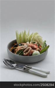 Spicy Stir Fried seafood Instant Noodles with herbs with various spices served with vegetables, cucumber, thai eggplant, chinese cabbage, white turmeric, winged bean and yardlong bean in ceramic plate. Copy space, Selective focus.